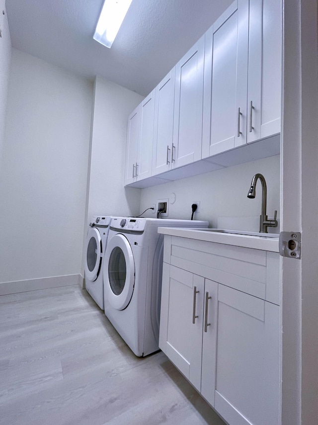 clothes washing area with sink, separate washer and dryer, light wood-type flooring, a textured ceiling, and cabinets