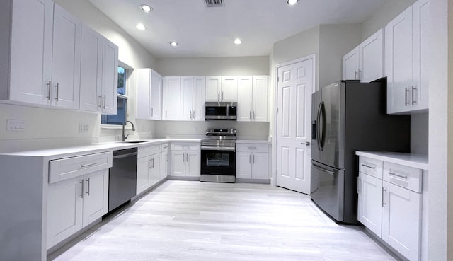 kitchen with light hardwood / wood-style floors, white cabinetry, stainless steel appliances, and sink