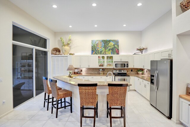 kitchen featuring white cabinets, a kitchen bar, stainless steel appliances, light stone countertops, and a center island with sink