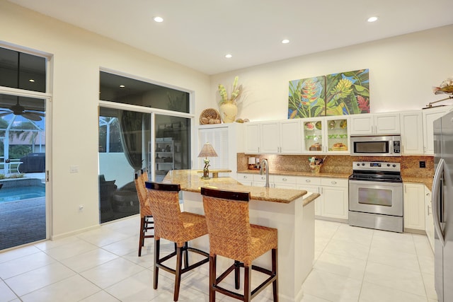 kitchen featuring a kitchen bar, a center island with sink, white cabinets, light stone counters, and stainless steel appliances