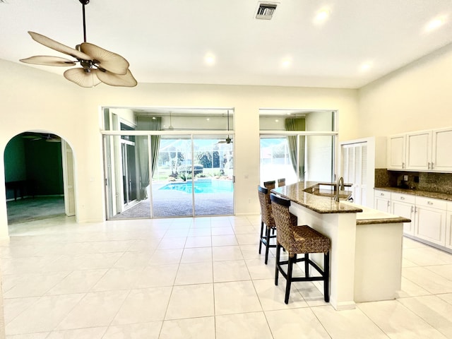 kitchen featuring tasteful backsplash, white cabinetry, dark stone countertops, a breakfast bar area, and a kitchen island with sink