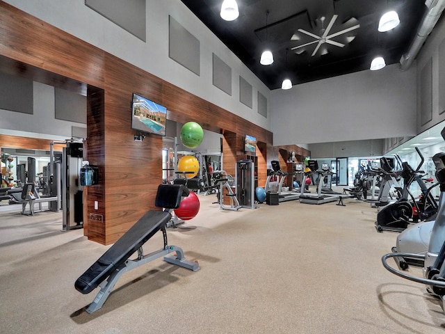 exercise room featuring carpet flooring, a high ceiling, and wooden walls