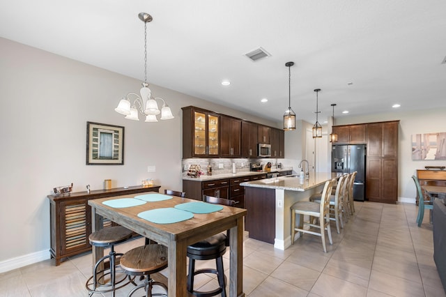 kitchen with decorative backsplash, stainless steel appliances, a center island with sink, sink, and pendant lighting