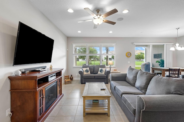 living room featuring a textured ceiling, light tile patterned floors, and ceiling fan with notable chandelier