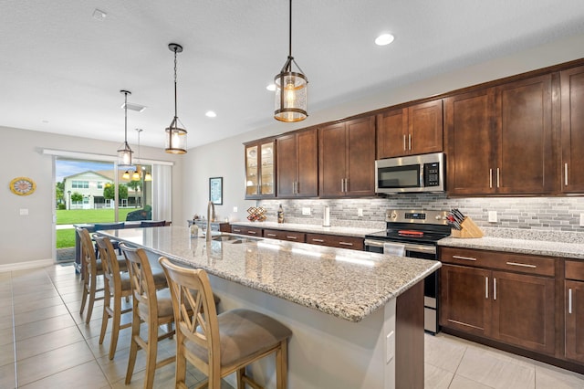 kitchen featuring a center island with sink, light stone counters, a breakfast bar area, sink, and stainless steel appliances