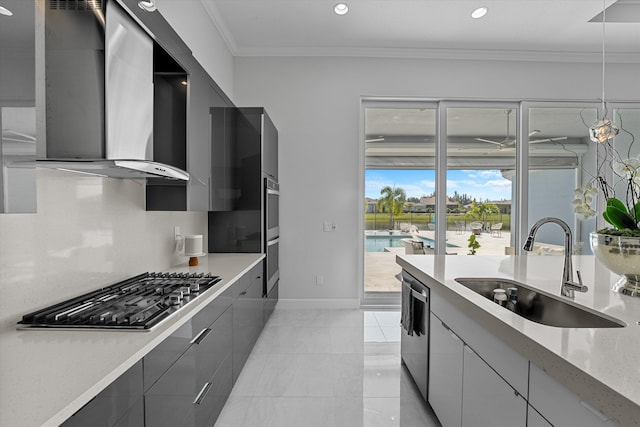 kitchen with sink, stainless steel appliances, wall chimney exhaust hood, decorative light fixtures, and ornamental molding