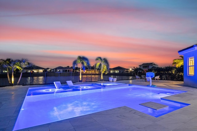 pool at dusk with an in ground hot tub and a patio area