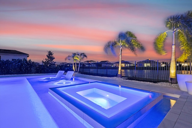 pool at dusk featuring an in ground hot tub