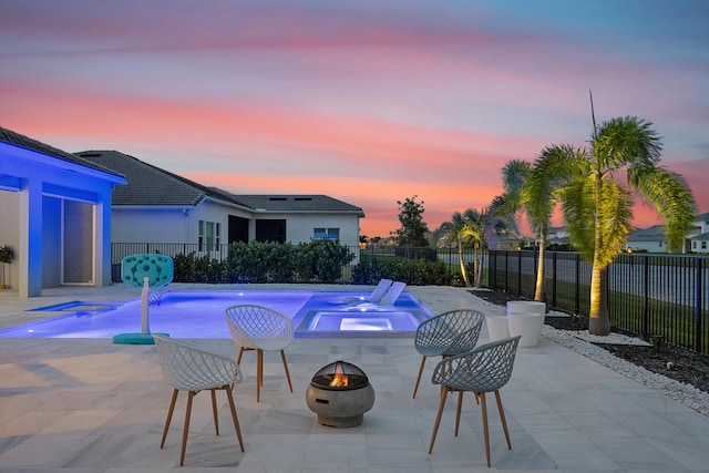 pool at dusk with an in ground hot tub, a patio area, pool water feature, and a fire pit