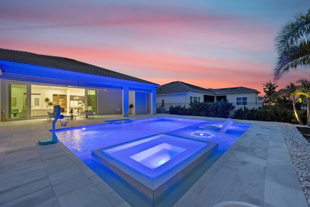 pool at dusk featuring an in ground hot tub and a patio