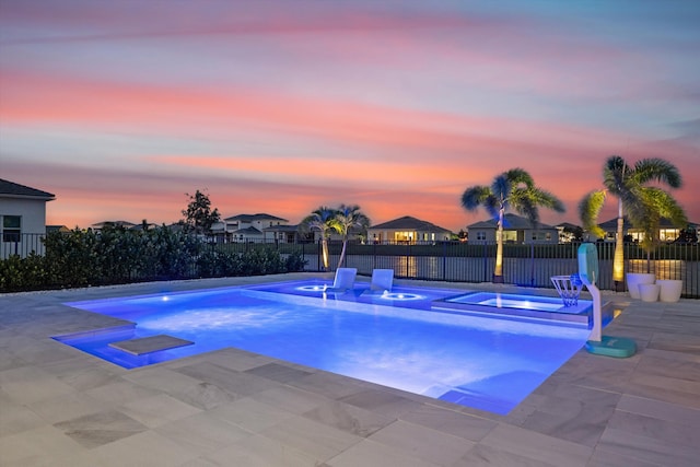 pool at dusk featuring a patio and an in ground hot tub