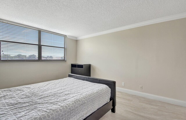 bedroom with a textured ceiling, ornamental molding, and light hardwood / wood-style flooring