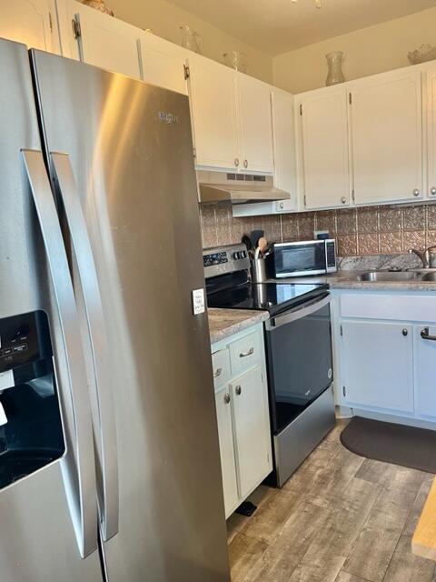 kitchen with appliances with stainless steel finishes, white cabinetry, sink, backsplash, and light hardwood / wood-style floors