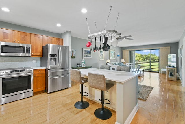 kitchen with decorative backsplash, a kitchen bar, stainless steel appliances, light hardwood / wood-style floors, and a center island