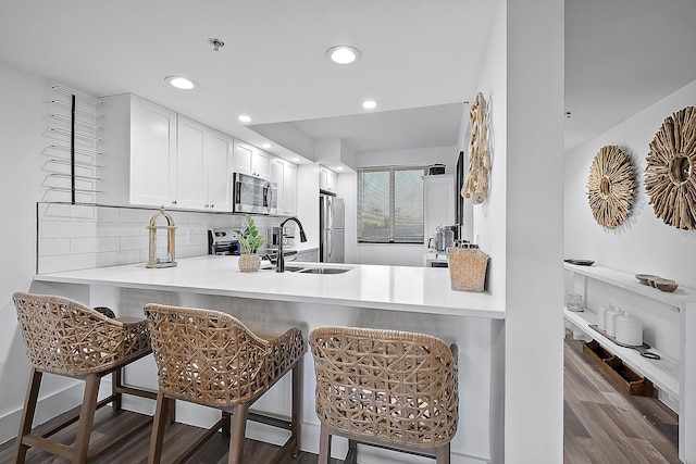 kitchen with kitchen peninsula, a kitchen breakfast bar, stainless steel appliances, white cabinets, and dark hardwood / wood-style floors