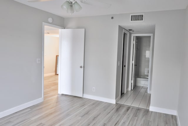 unfurnished bedroom with a closet, ensuite bathroom, light wood-type flooring, and ceiling fan