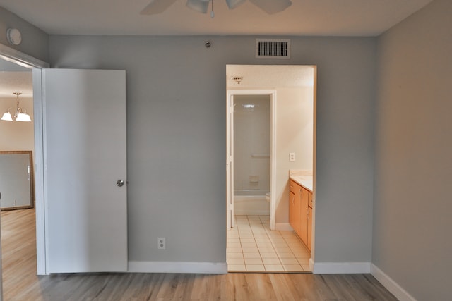 unfurnished bedroom featuring light hardwood / wood-style flooring, ensuite bathroom, and ceiling fan with notable chandelier