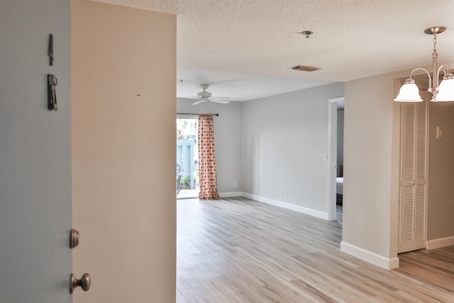 empty room featuring a textured ceiling, ceiling fan with notable chandelier, and light wood-type flooring