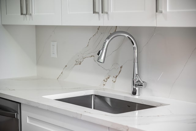 room details featuring light stone counters, sink, stainless steel dishwasher, and white cabinets