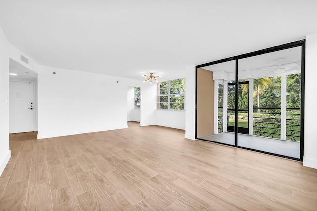 unfurnished room featuring light wood-type flooring, an inviting chandelier, plenty of natural light, and floor to ceiling windows