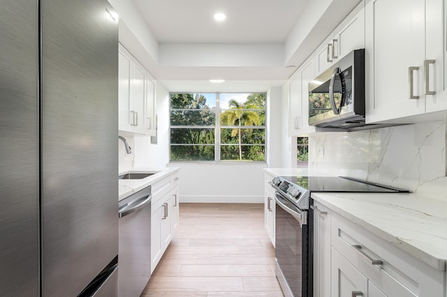 kitchen featuring appliances with stainless steel finishes, light hardwood / wood-style flooring, white cabinetry, and light stone counters