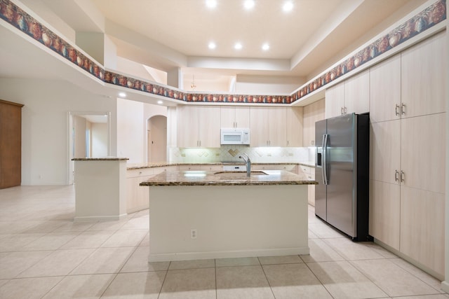 kitchen featuring light stone countertops, stainless steel refrigerator with ice dispenser, a kitchen island with sink, sink, and light tile patterned floors