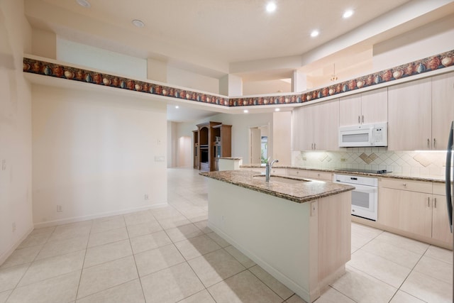 kitchen with white appliances, sink, decorative backsplash, an island with sink, and stone countertops