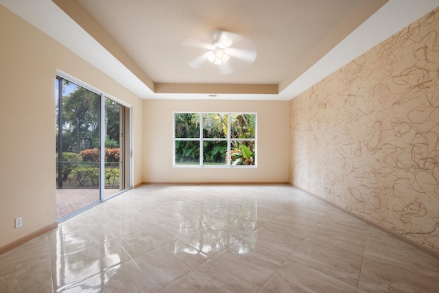 spare room featuring plenty of natural light, ceiling fan, and a raised ceiling