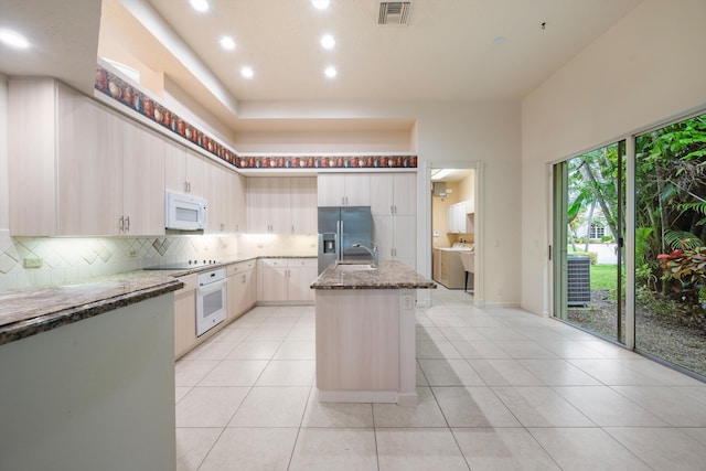 kitchen featuring light stone countertops, sink, an island with sink, white appliances, and light tile patterned floors