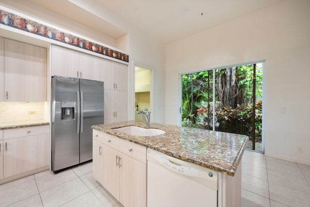 kitchen featuring stainless steel fridge, light stone counters, white dishwasher, sink, and a center island with sink