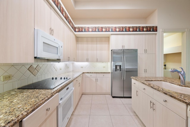 kitchen with light stone countertops, light brown cabinetry, backsplash, white appliances, and sink