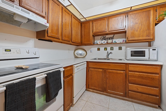 kitchen featuring white appliances, brown cabinets, light countertops, under cabinet range hood, and a sink