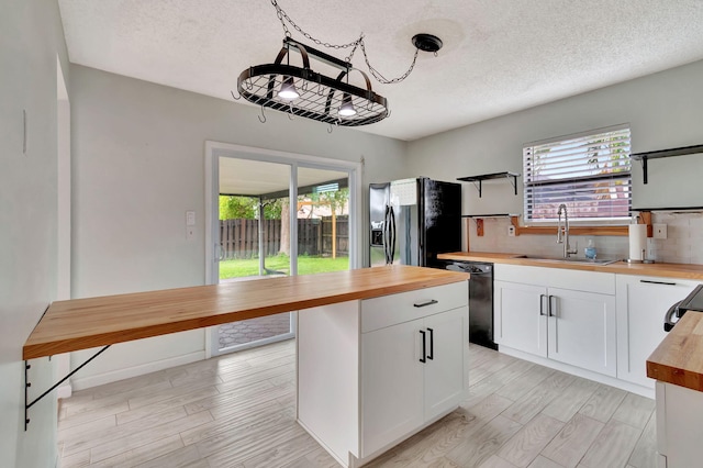 kitchen featuring a wealth of natural light, sink, butcher block counters, and white cabinetry