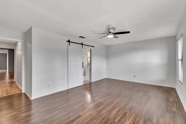 empty room with dark hardwood / wood-style floors, a barn door, a textured ceiling, and ceiling fan