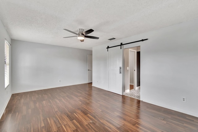 unfurnished room with a textured ceiling, a barn door, ceiling fan, and dark hardwood / wood-style flooring