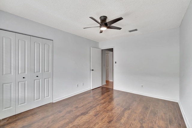 unfurnished bedroom with a closet, a textured ceiling, dark wood-type flooring, and ceiling fan