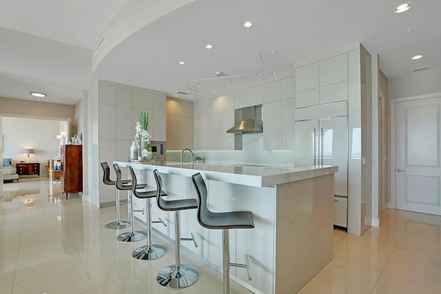 kitchen featuring a kitchen breakfast bar, white cabinetry, wall chimney exhaust hood, and a spacious island