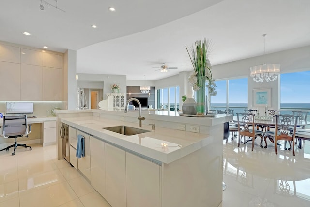 kitchen with sink, light stone counters, pendant lighting, a center island with sink, and ceiling fan with notable chandelier