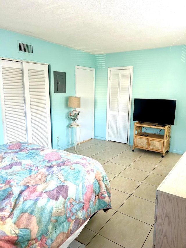 bedroom with a textured ceiling, electric panel, two closets, and light tile patterned floors