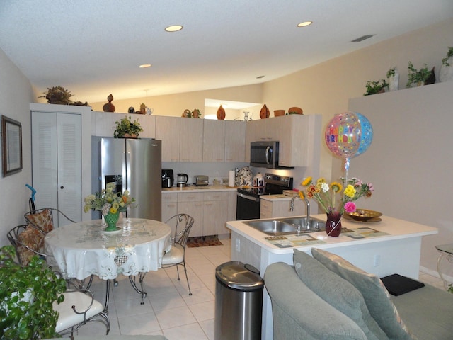 kitchen with appliances with stainless steel finishes, a center island, lofted ceiling, light tile patterned floors, and light brown cabinets