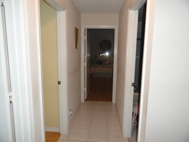 hallway with a textured ceiling and light tile patterned flooring