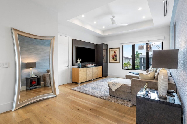 living room with ceiling fan, a raised ceiling, and wood-type flooring