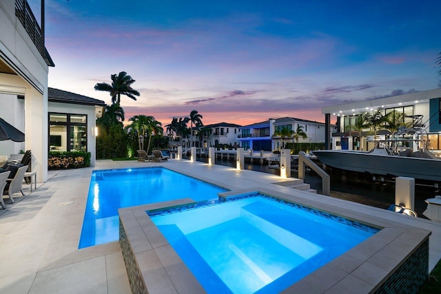 pool at dusk featuring an in ground hot tub and a patio