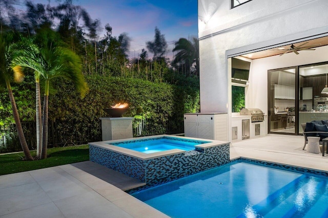 pool at dusk featuring an in ground hot tub, area for grilling, a patio area, exterior kitchen, and ceiling fan