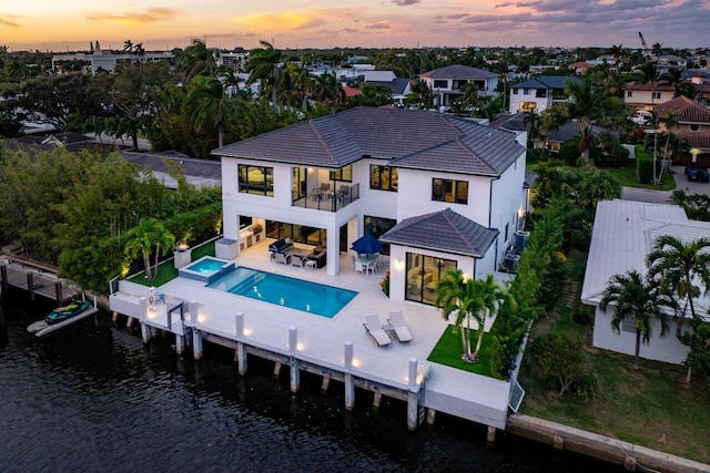 back house at dusk with cooling unit, a patio, outdoor lounge area, a water view, and a balcony