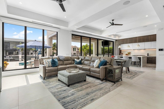 living room with ceiling fan, a raised ceiling, and light tile patterned floors