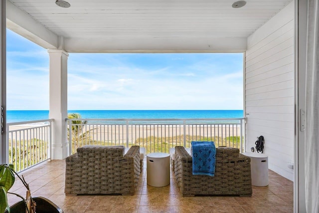 interior space featuring a balcony, a water view, and a beach view