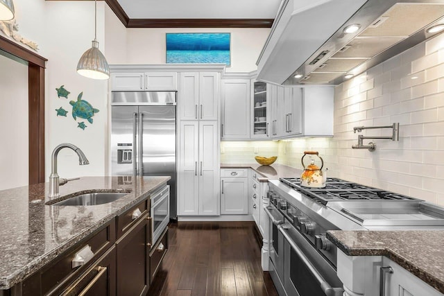 kitchen with sink, wall chimney range hood, dark hardwood / wood-style floors, built in appliances, and white cabinets