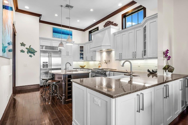 kitchen with premium range hood, sink, built in refrigerator, dark hardwood / wood-style floors, and decorative light fixtures