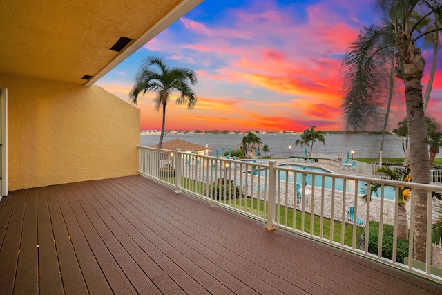 deck at dusk featuring a fenced in pool and a water view